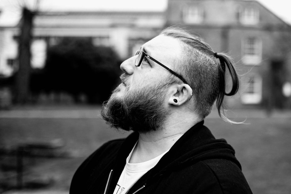 Nathan Pearson in profile, bearded, glasses, hair tied back, looking up. Black and white.